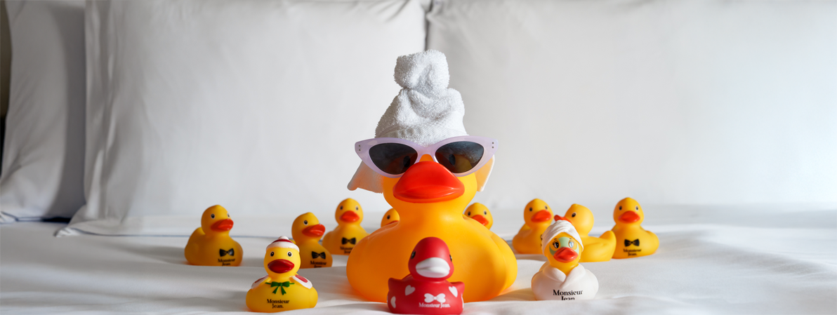 Canard de bain avec lunettes entouré de petits canards dans une chambre d’hôtel au design moderne