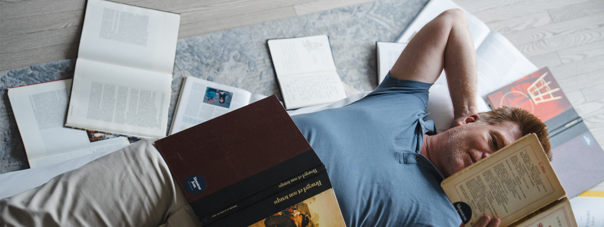 Homme allongé sur un lit lisant un livre dans une chambre d’hôtel confortable et lumineuse