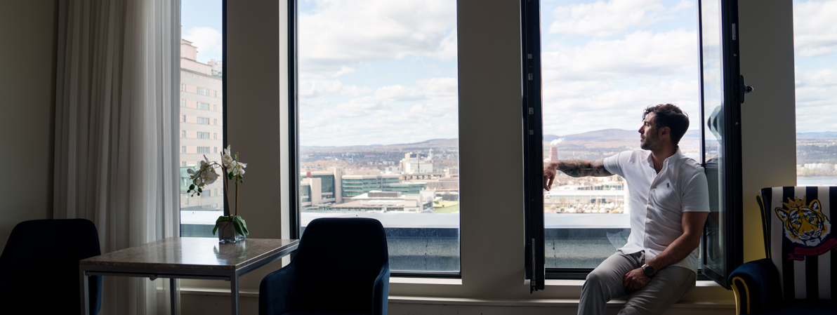 Homme assis près d’une grande fenêtre avec vue panoramique sur la ville de Québec depuis une chambre d’hôtel