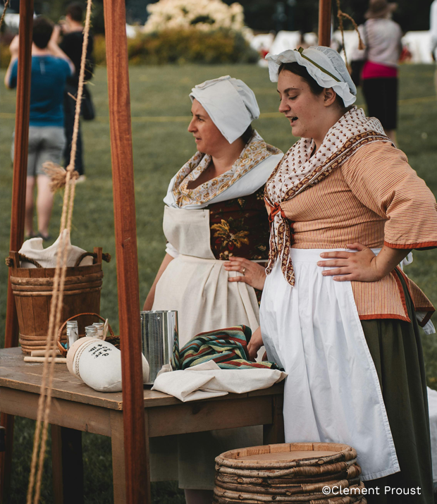 Personnes en costumes d’époque participant aux Fêtes de la Nouvelle-France, autour d’un kiosque extérieur dans une ambiance historique et conviviale.