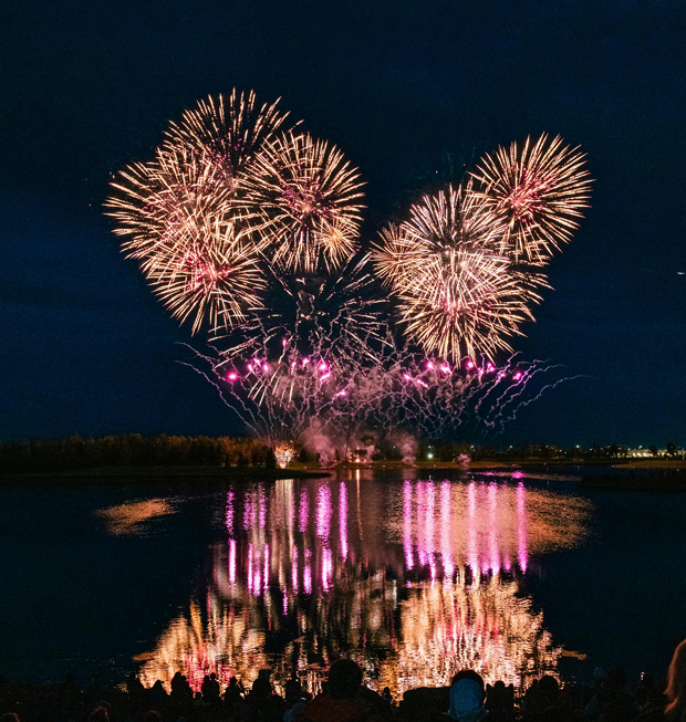 Feux d’artifice illuminant le ciel nocturne au-dessus du fleuve Saint-Laurent, avec leurs reflets colorés sur l’eau et des spectateurs rassemblés au premier plan lors des Grands Feux Loto-Québec.