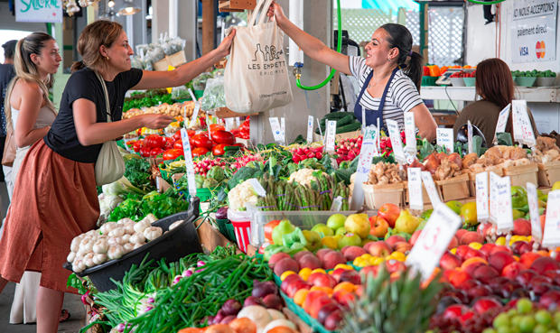 Grand Marché de Québec animé avec des étals colorés de fruits et légumes frais, où des clients échangent avec des marchands dans une ambiance conviviale et locale.
