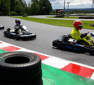 Personnes faisant du karting sur une piste extérieure, portant des casques colorés et roulant côte à côte dans une ambiance sportive et dynamique.