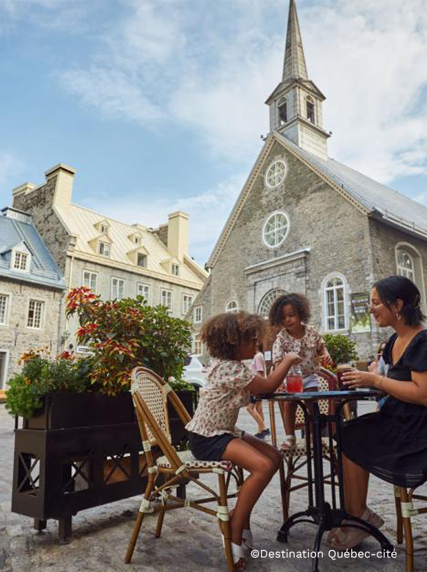 Famille profitant d’une terrasse dans le Vieux-Québec devant une église historique en pierre, dans une ambiance estivale et conviviale.