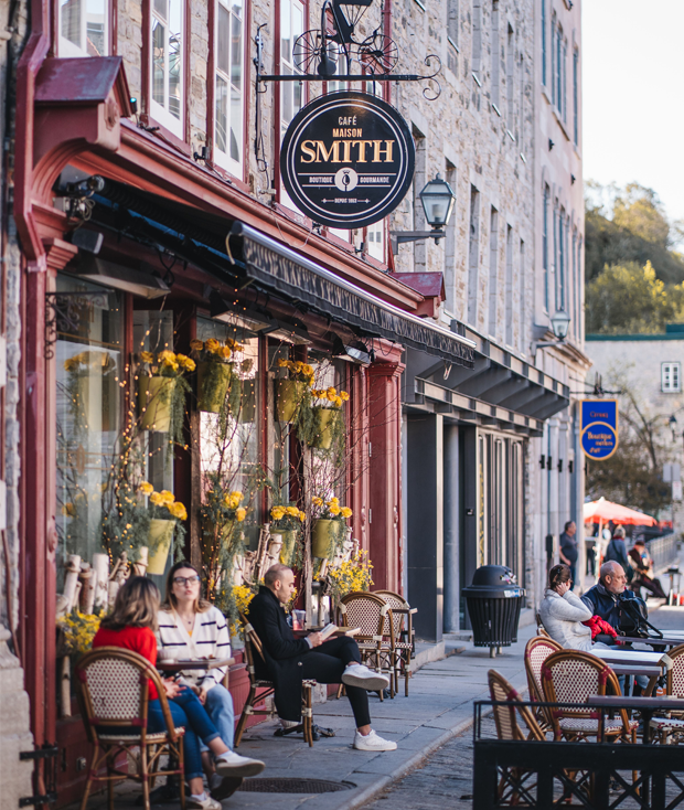 The First Spring Terraces in Old Québec Café terrace on a cobblestone street in Old Québec, in front of a stone façade decorated with spring flowers.