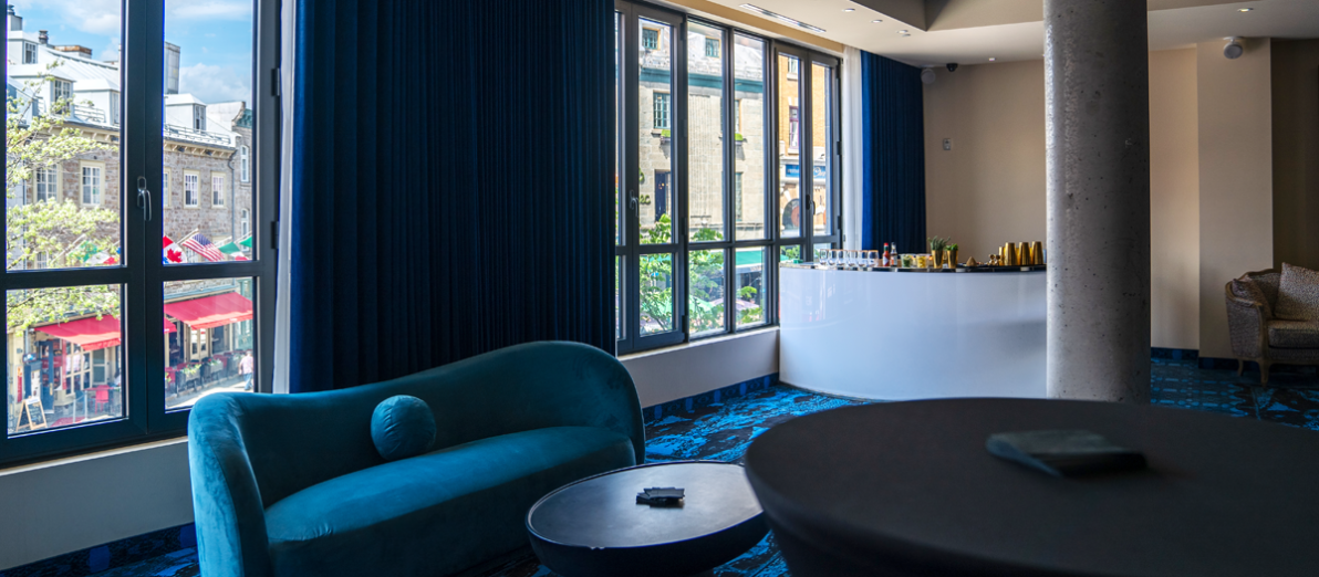 Espace cocktail avec bar, mobilier lounge et grandes fenêtres donnant sur la rue Saint-Jean à l'Hôtel Monsieur Jean dans le Vieux-Québec.